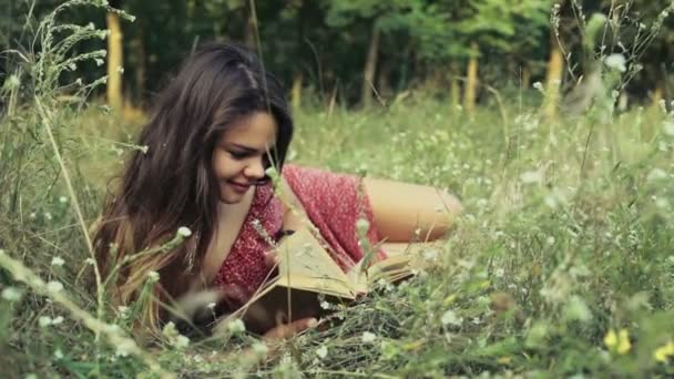 Ung kvinna innehåller i fältet blommor och läser en bok Slowmotion — Stockvideo