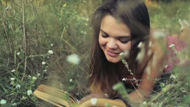 Ung kvinna innehåller i fältet blommor och läser en bok Slowmotion — Stockvideo