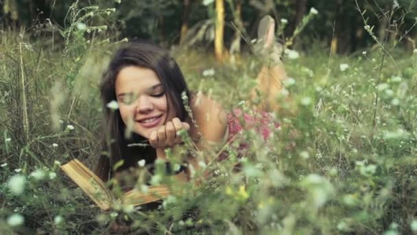 Молодая женщина лежит в полевых цветах и читает книгу замедленной съемки — стоковое видео