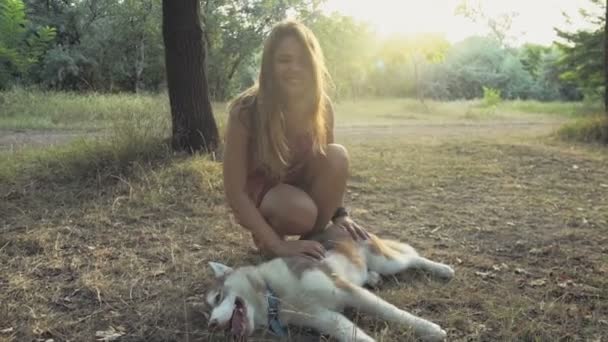 Joven mujer acaricia un husky perro y mira en cámara en bosque cámara lenta — Vídeos de Stock