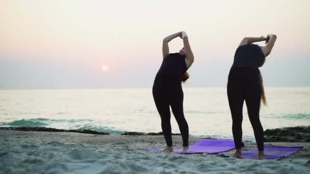 Dos hembras jóvenes practican yoga en la playa cámara lenta — Vídeos de Stock