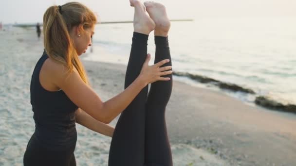 To unge kvinner øver yoga på stranden. Langsom bevegelse. – stockvideo