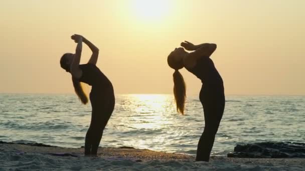 Две молодые женщины практикуют йогу на пляже замедленной съемки — стоковое видео