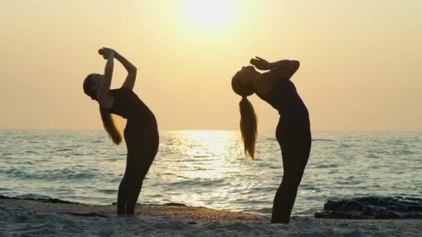 Dos hembras jóvenes practican yoga en la playa cámara lenta — Vídeos de Stock