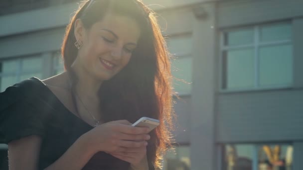 Elegante dame maakt gebruik van een smartphone en glimlacht in de straat slow motion — Stockvideo