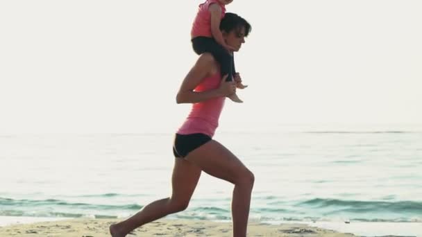 Moeder met een kind op haar schouders doet squats op het strand slow motion — Stockvideo