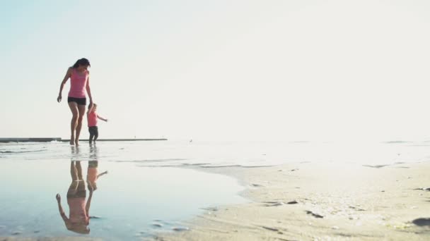 Moeder en haar kind lopen langs het strand slow motion — Stockvideo