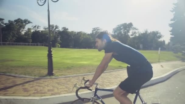 Young handsome man rides a bicycle in the park slow motion — Stock Video