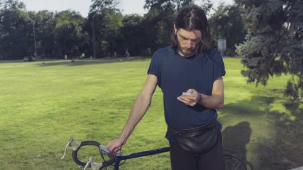 Joven se para cerca de la bicicleta y utiliza el teléfono inteligente de cámara lenta — Vídeos de Stock