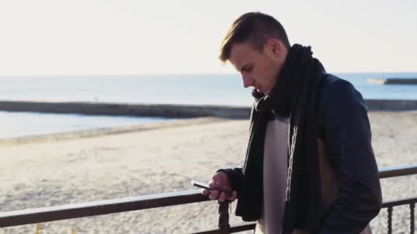 Jovem usando um smartphone na praia de outono — Vídeo de Stock