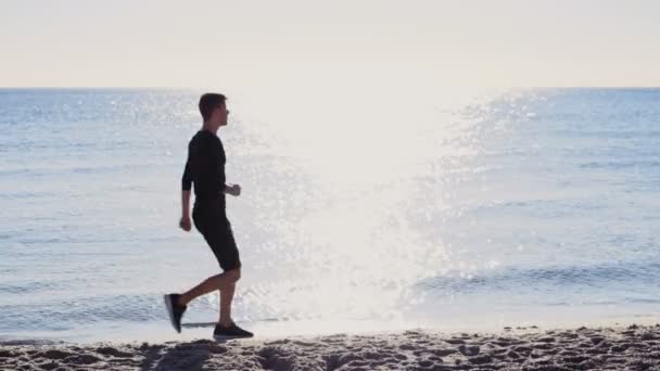 Mannelijke atleet gestopt om te genieten van het uitzicht op de zee en de zon op het strand — Stockvideo