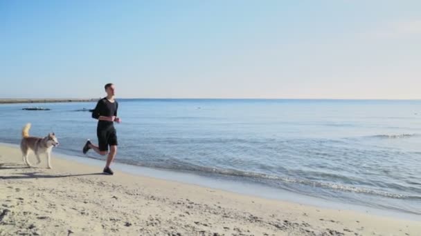 Młodego sportowca i jego pies biegnąc wzdłuż plaży zwolnionym tempie — Wideo stockowe