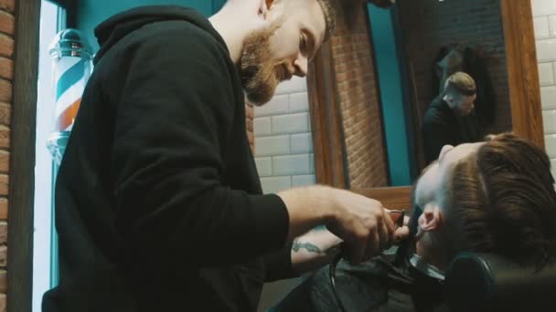 Парикмахер бреет бороду клиента триммером — стоковое видео