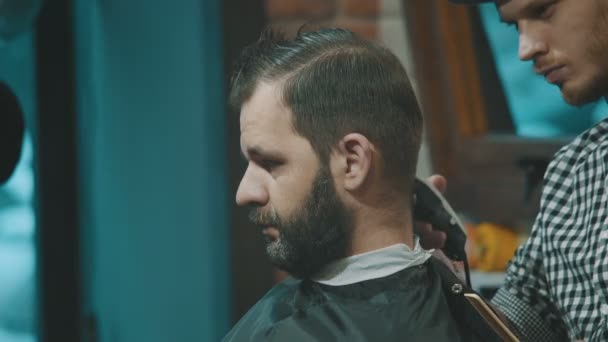 Peluquero corta el cabello del cliente con un cortador — Vídeo de stock