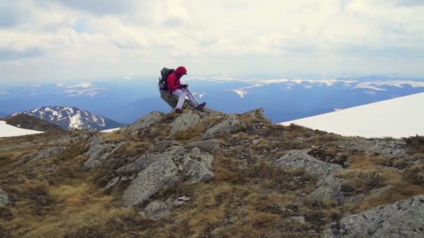 Excursionista sentado en las rocas contra el paisaje montañoso — Vídeos de Stock