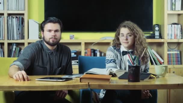 Par elever sitter i klassrummet och tittar på kameran — Stockvideo