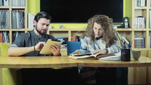 Manlig student använder tablet bredvid kvinna läser böcker ultrarapid — Stockvideo