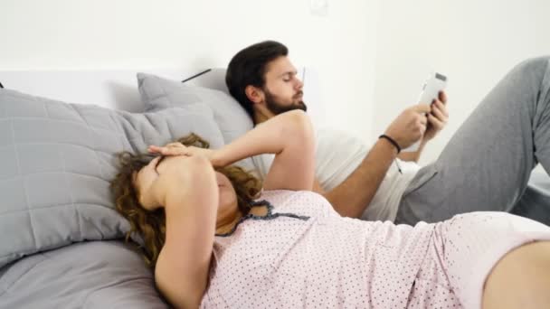 Ospalý žena a muž, pomocí tabletu v posteli zpomalené — Stock video