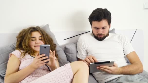 Pasangan di tempat tidur menggunakan smartphone dan tablet gerak lambat — Stok Video