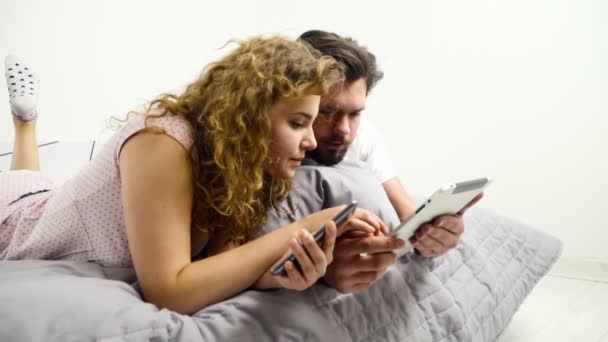 Мужчина и женщина, используя свои гаджеты в постели замедленной съемки — стоковое видео