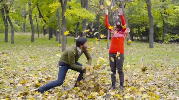 Young couple throwing up the fallen leaves in the park slow motion — Stock Video