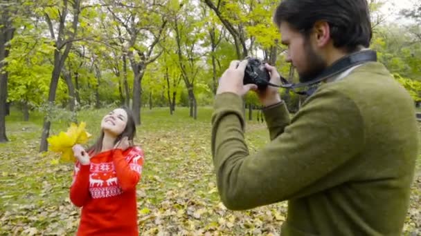 Mannelijke nemen van foto's van een jonge vrouw in het najaar park Slowmotion — Stockvideo