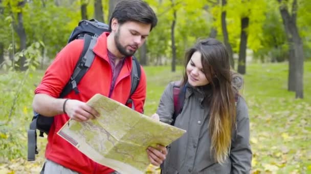 Ζευγάρι των backpackers κοιτάζοντας το χάρτη χαρτί στο φθινόπωρο δάσος — Αρχείο Βίντεο