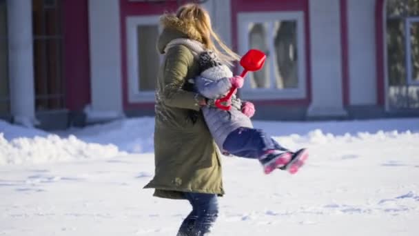 Mãe girando com sua filha nos braços na neve câmera lenta — Vídeo de Stock