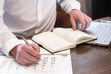 Adamın elleri, dizüstü bilgisayarın arka planında ve takvimde. Evden çalış.