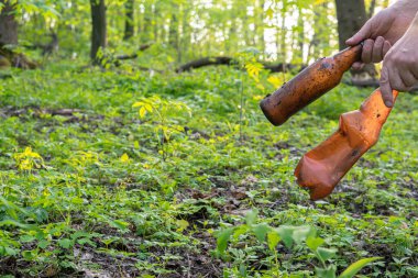 Adamın eli ormanda çöp topluyor, elinde de kirli bir şişe.