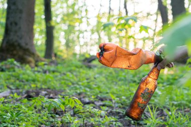 Adamın eli ormanda çöp topluyor, elinde de kirli bir şişe.