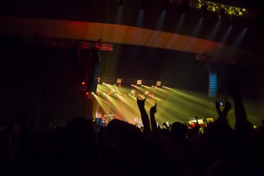 Parlak sahne ışıkları önünde konser kalabalığının siluetleri