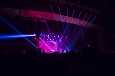 Parlak sahne ışıkları önünde konser kalabalığının siluetleri
