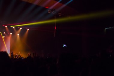 Parlak sahne ışıkları önünde konser kalabalığının siluetleri