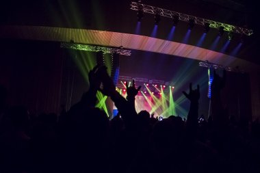 Parlak sahne ışıkları önünde konser kalabalığının siluetleri