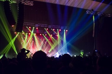 Parlak sahne ışıkları önünde konser kalabalığının siluetleri