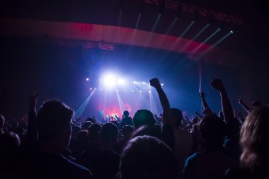 Parlak sahne ışıkları önünde konser kalabalığının siluetleri
