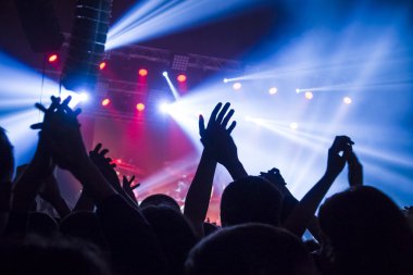 Parlak sahne ışıkları önünde konser kalabalığının siluetleri
