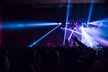 Parlak sahne ışıkları önünde konser kalabalığının siluetleri
