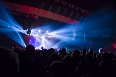 Parlak sahne ışıkları önünde konser kalabalığının siluetleri