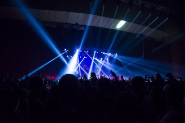 Parlak sahne ışıkları önünde konser kalabalığının siluetleri