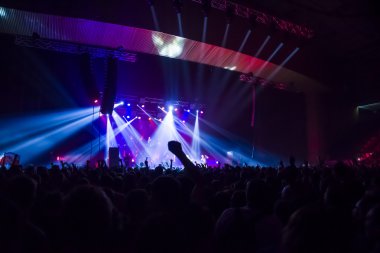 Parlak sahne ışıkları önünde konser kalabalığının siluetleri