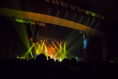 Parlak sahne ışıkları önünde konser kalabalığının siluetleri