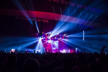 Parlak sahne ışıkları önünde konser kalabalığının siluetleri
