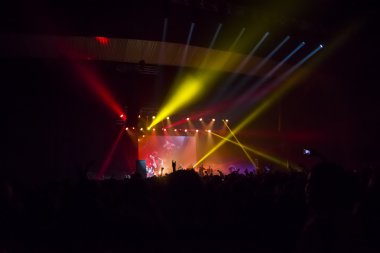 Parlak sahne ışıkları önünde konser kalabalığının siluetleri