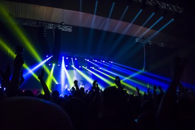 Parlak sahne ışıkları önünde konser kalabalığının siluetleri