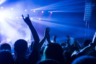 Parlak sahne ışıkları önünde konser kalabalığının siluetleri