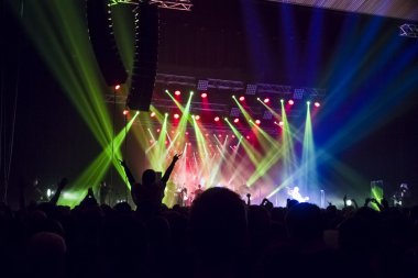 Parlak sahne ışıkları önünde konser kalabalığının siluetleri