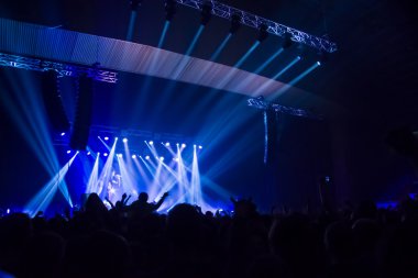Parlak sahne ışıkları önünde konser kalabalığının siluetleri