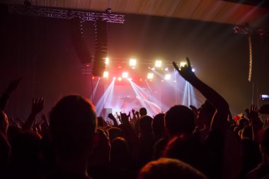 Parlak sahne ışıkları önünde konser kalabalığının siluetleri